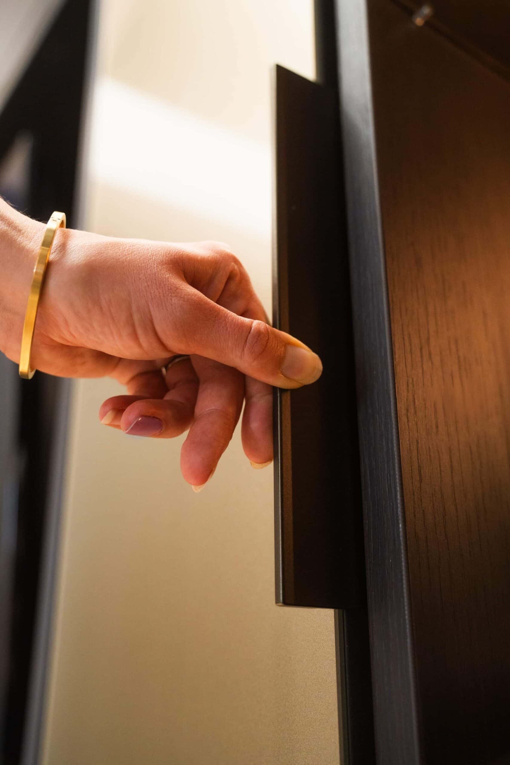Hand opening a dark wardrobe door by its recessed handle
