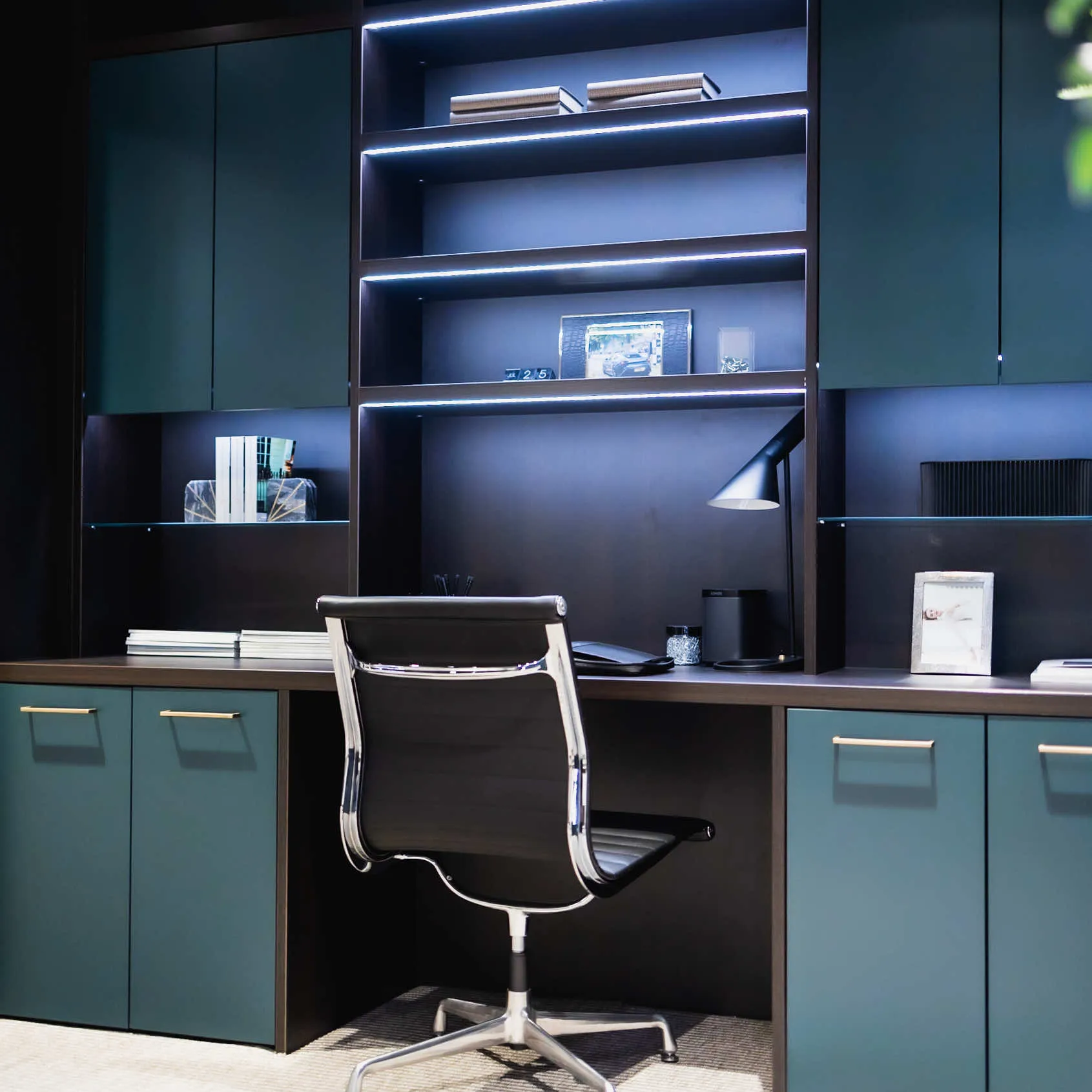 Study with teal doors, dark desk, LED-lit shelving and a black office chair