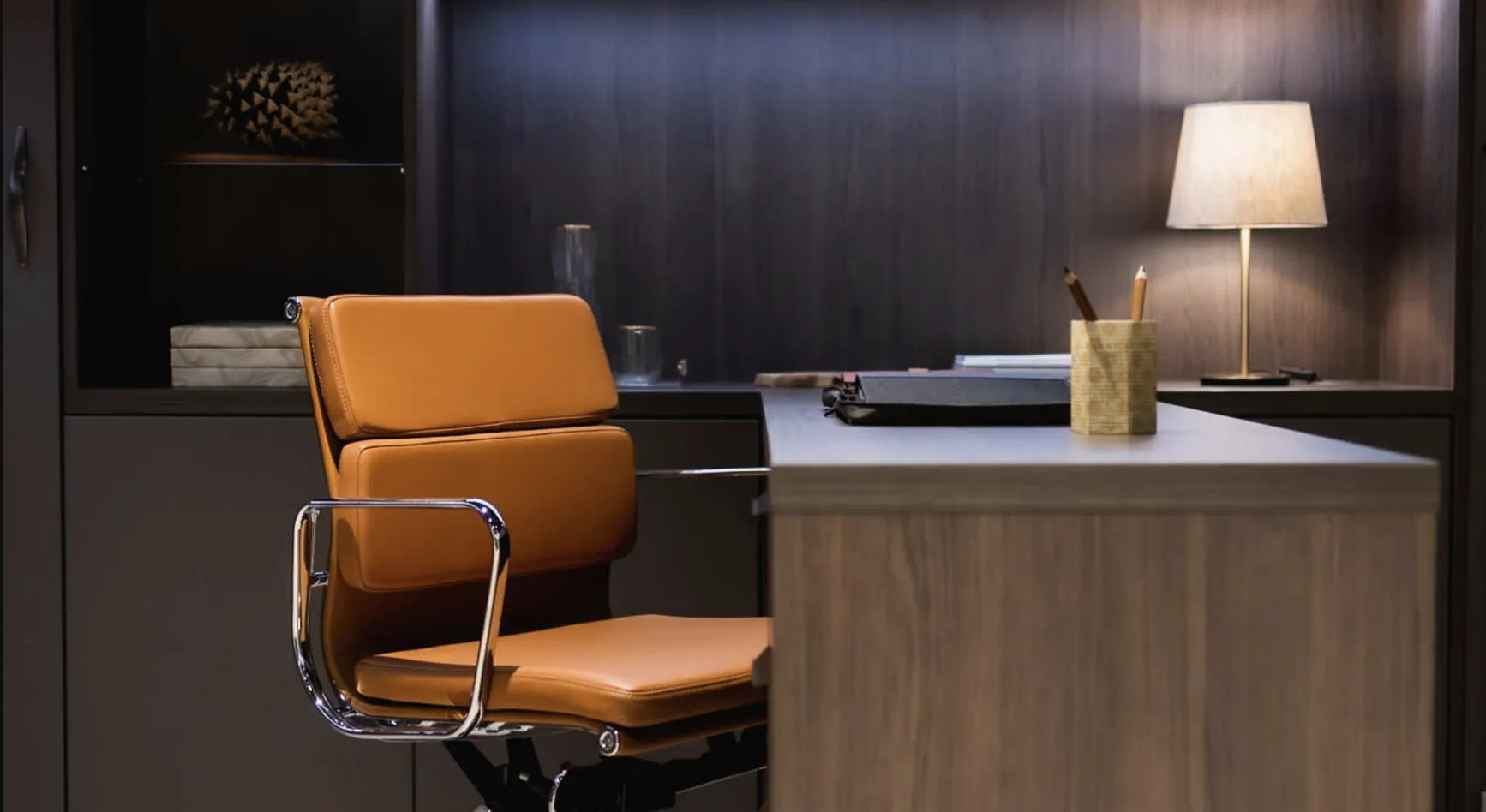 Tan leather office chair at a wood-veneer desk with a table lamp