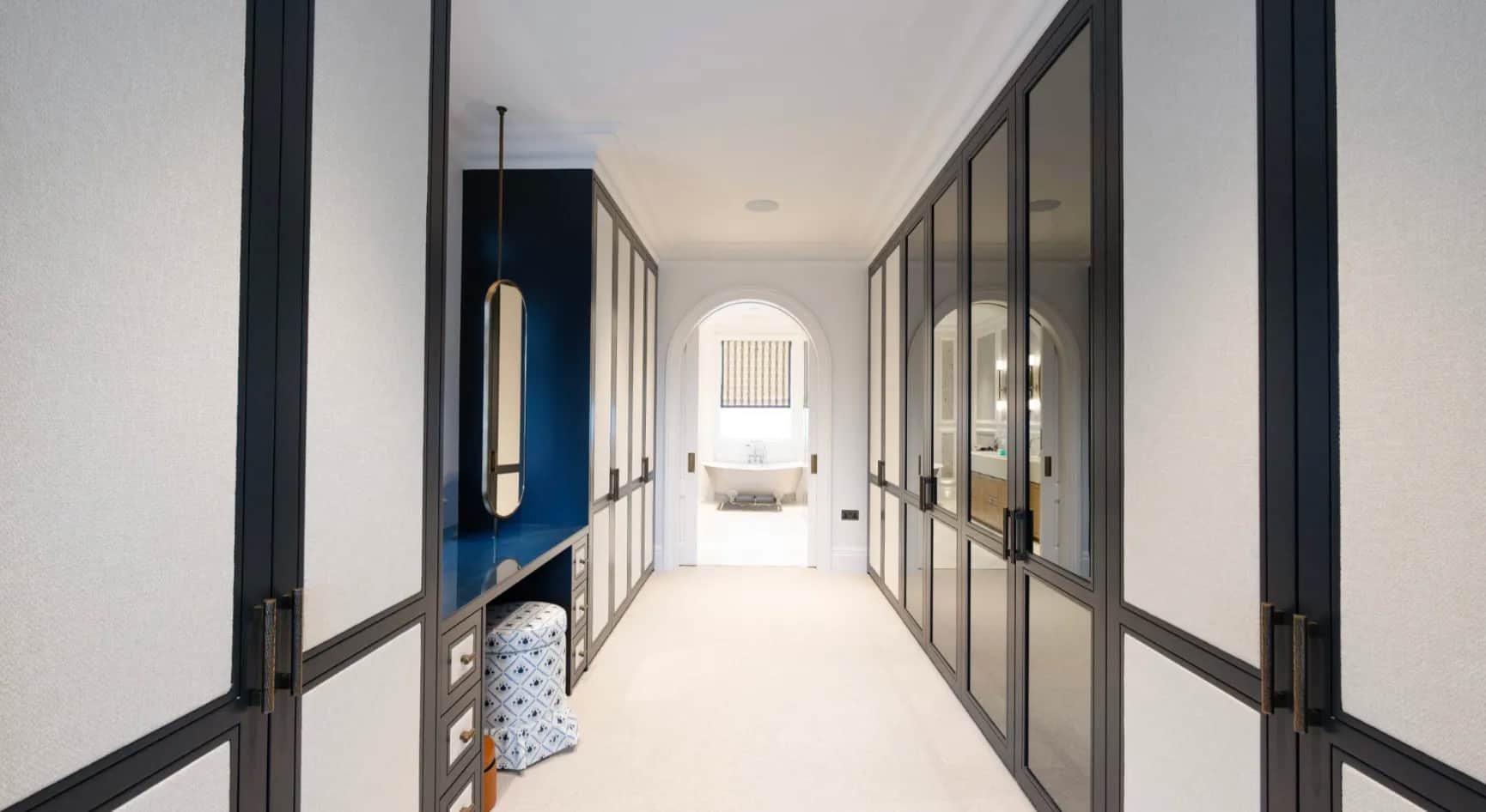 Dressing room corridor with glazed black-framed wardrobe doors and a navy dressing table