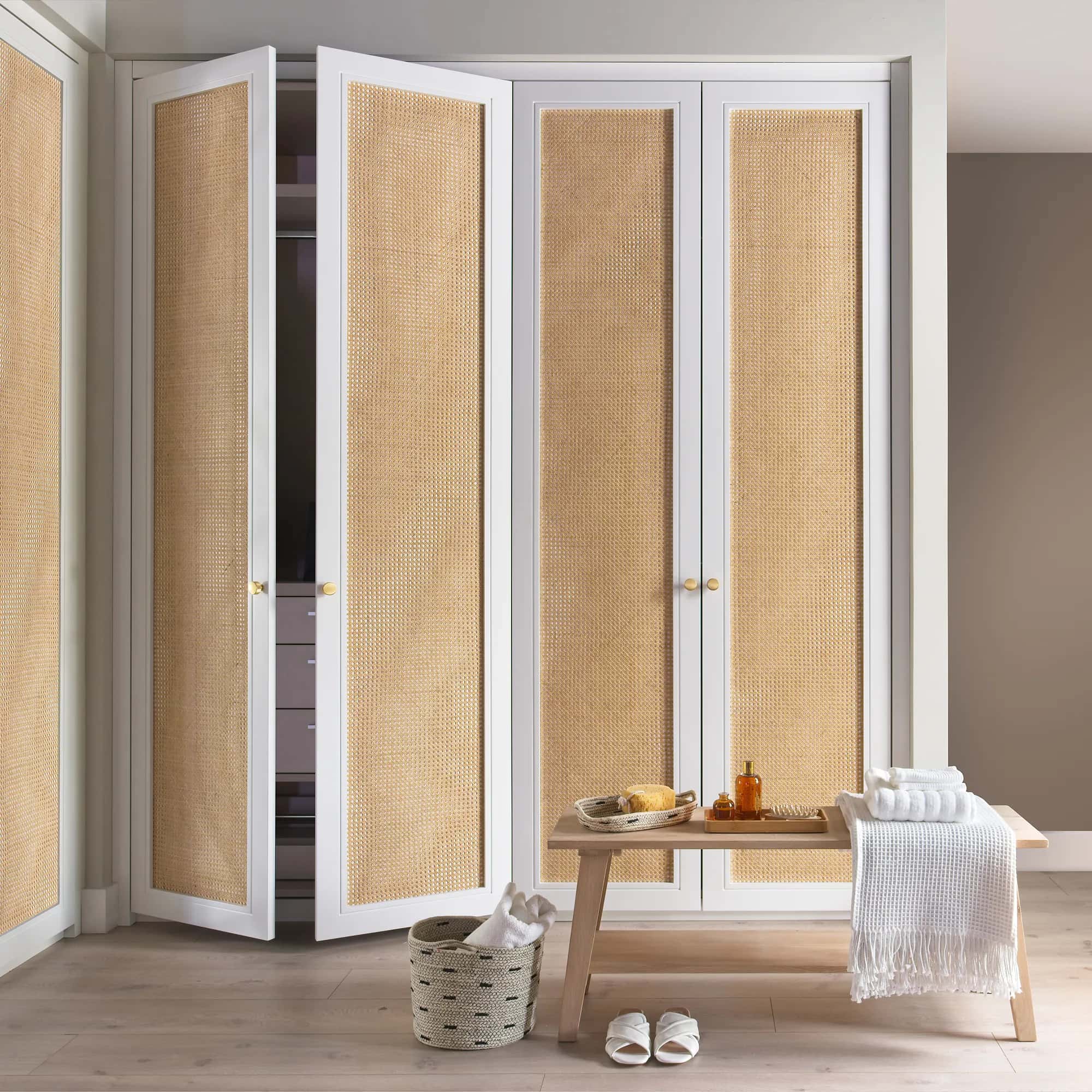 Fitted wardrobe with white frames and rattan cane panel doors, brass knobs and a bench