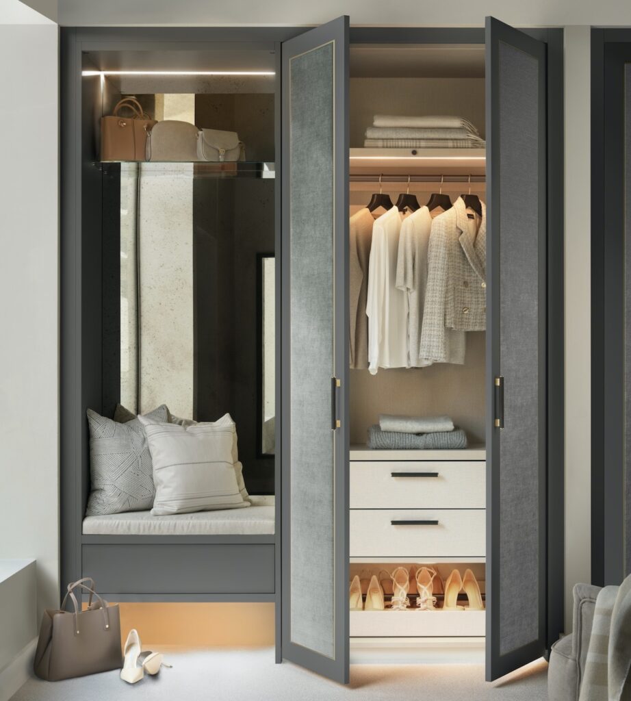 Mirror and bench seat with dark grey painted wood and light grey fabric panelled Belgravia style wardrobe doors open lifestyle image.