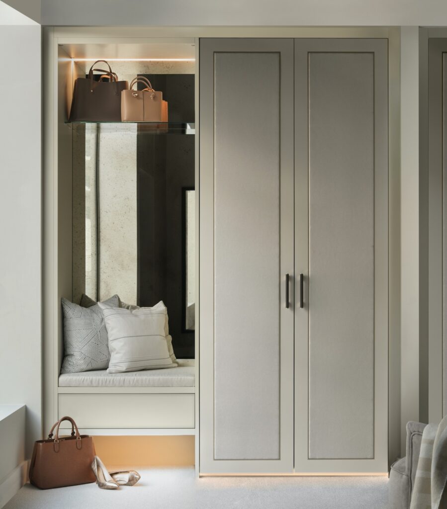 Mirror and bench seat with very pale grey painted wood and light grey fabric panelled Belgravia style wardrobe lifestyle image.